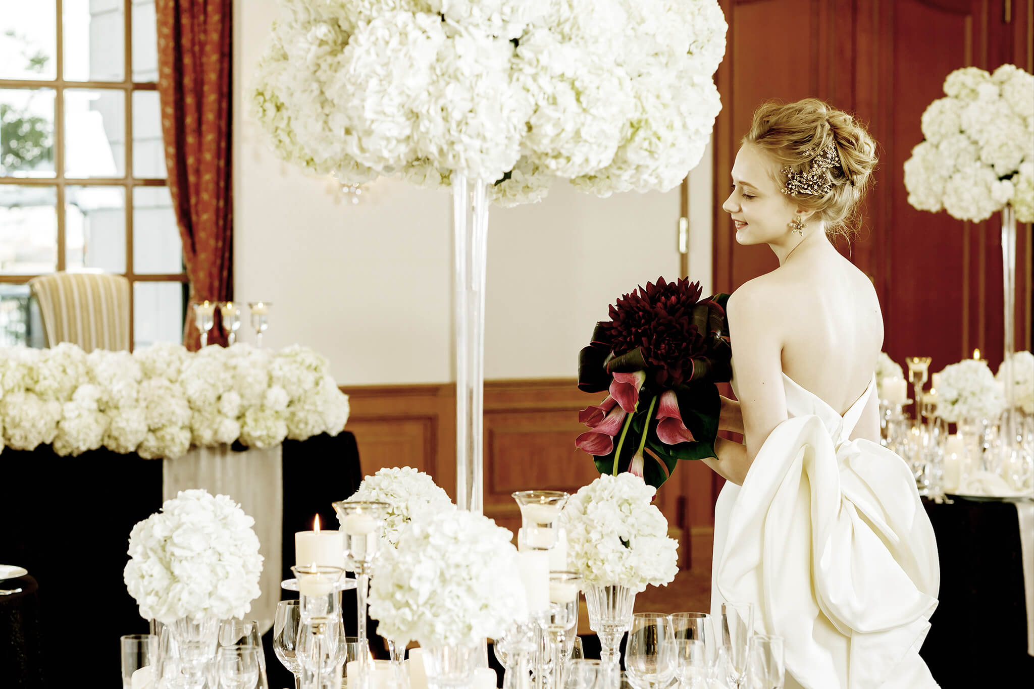 真っ白な装花に包まれた結婚式・披露宴会場の中をウェディングドレス姿で歩く新婦の様子